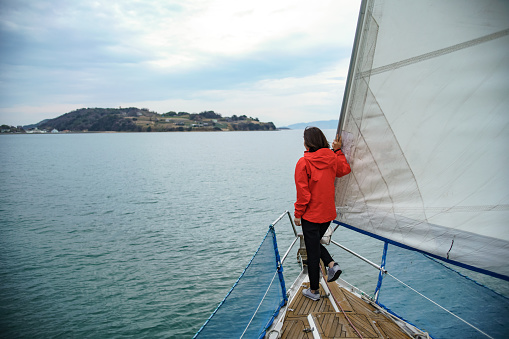 Mid adult woman using on the bow of a yacht as it sails towards an island