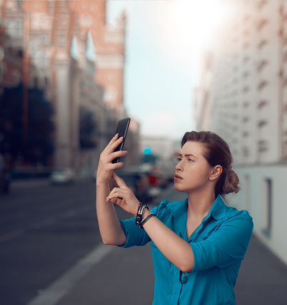 lifestyle shot of young woman in the city holding her smartphone and looking for signal.communication concept.