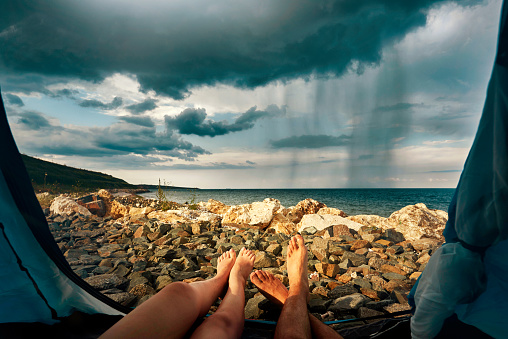 unrecognizable woman and man legslying down in tent at the edge of the sea, relaxing in spring day.cloudy and stormy weather.
