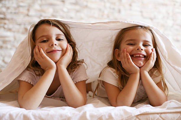 Two little girl in bed. Two little girl laying in bed and looking at camera. sister stock pictures, royalty-free photos & images