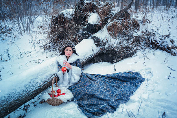Portrait of young woman dressed in blue coat. She is walking in the winter forest holding a basket with apples
