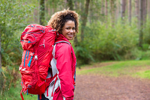 Female hiker is posing for the camera. She is wearing sports clothing and a backpack and is smiling at the camera.