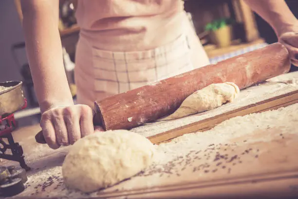 Close up of female baker hands kneading dough and making bread with a rolling pin. Retro look.