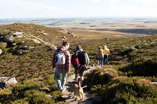 Group of people walking along a stone path in the hills. A pet dog is walking behind them.