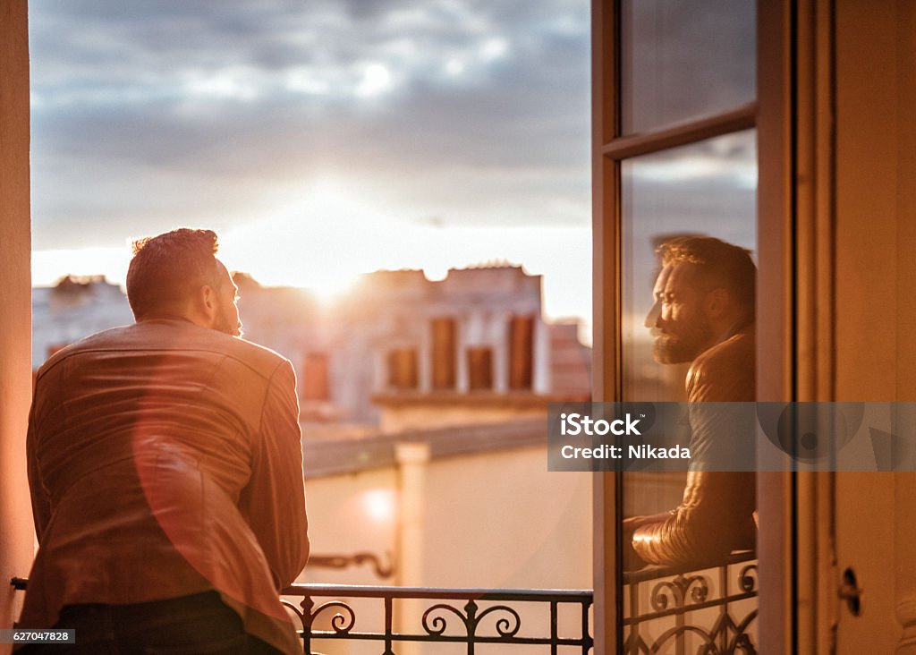 bearded man looking out over the city at sunrise bearded man looking out over the city at sunrise and reflecting himself in window glass Paris - France Stock Photo