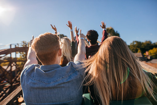 Rear view shot of young people on a thrilling roller coaster ride at amusement park. Group of friends having fun at fair and enjoying on a ride.