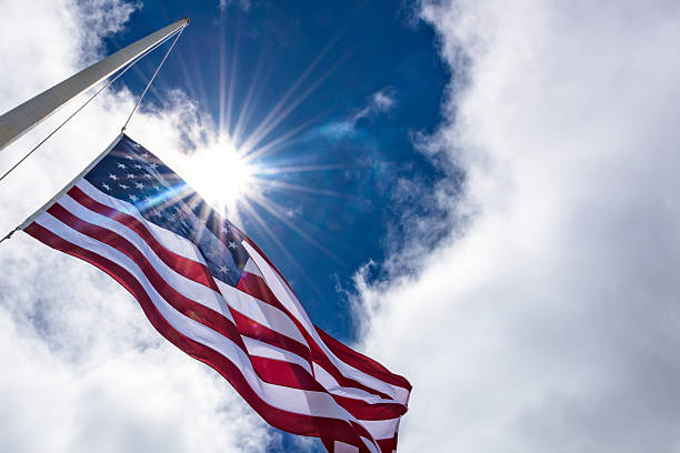 United States flag at half mast, looking up with sun stock photo