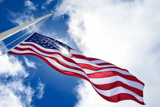 Photo of United States flag at half mast, looking up with sun