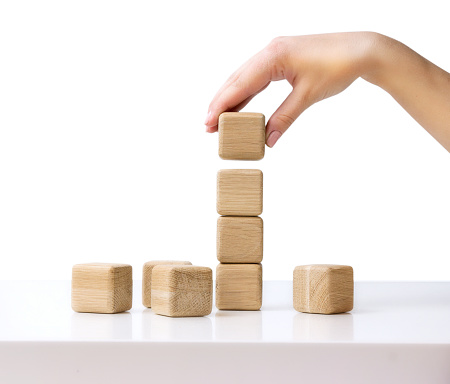 Stack of wooden blocks on white table isolated business concept.Hand establishes cube in a raw.Financial growth success.Building tower process.