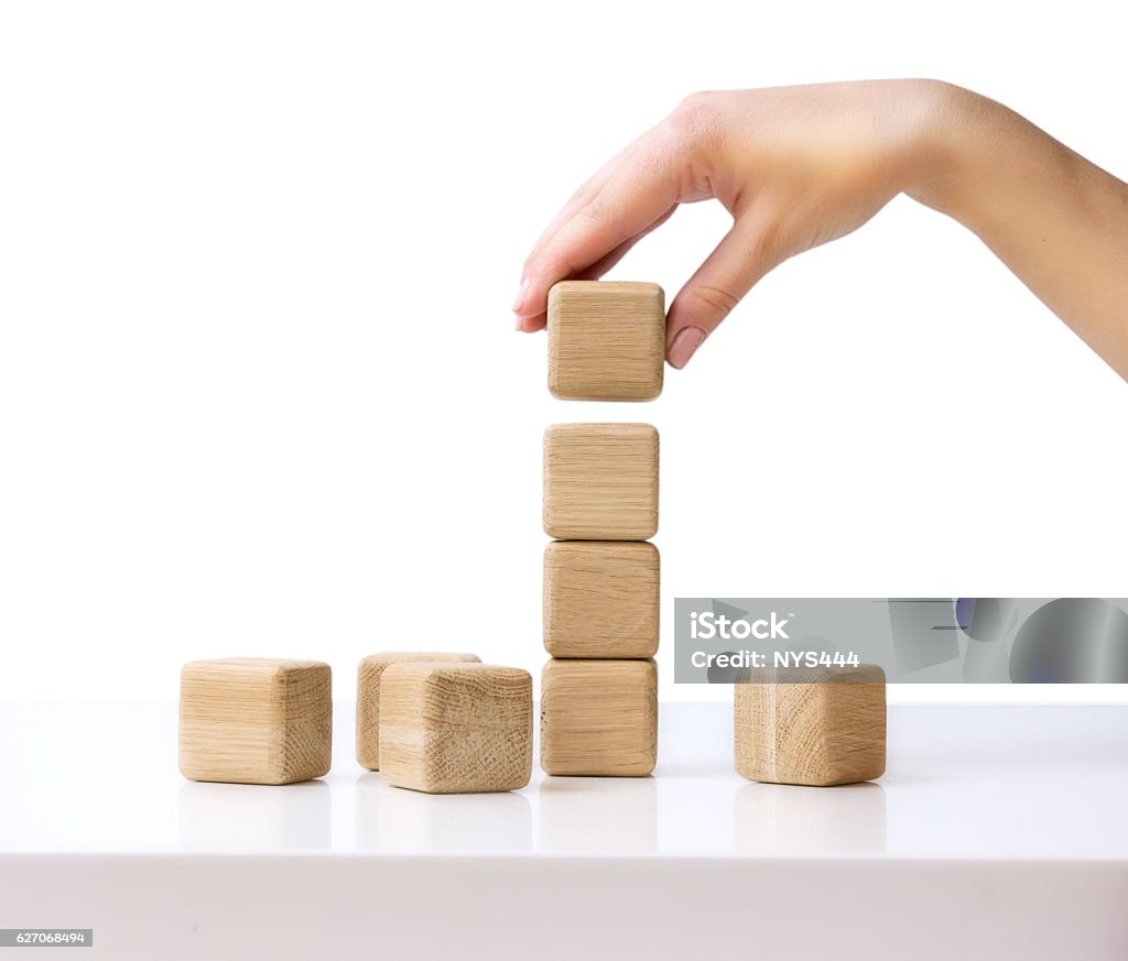 Stack wooden cubes.Hand establishes block tower isolated. Stack of wooden blocks on white table isolated business concept.Hand establishes cube in a raw.Financial growth success.Building tower process. Toy Block Stock Photo