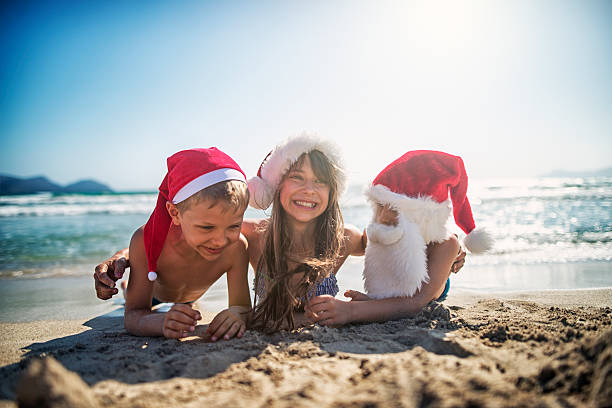 Christmas on the beach It's christmas on the beach. Kids wearing santa hats having fun on beach - laughing on wet sand. girls laying on beach stock pictures, royalty-free photos & images
