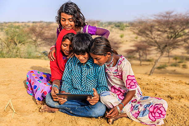 istock Happy Indian children using digital tablet, desert village, India 627071220