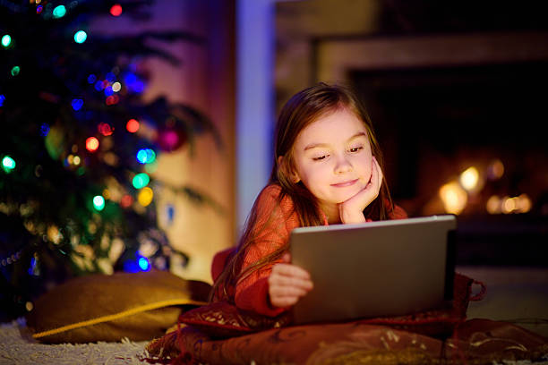 istock Adorable little girl using tablet pc by fireplace on Christmas 627071332