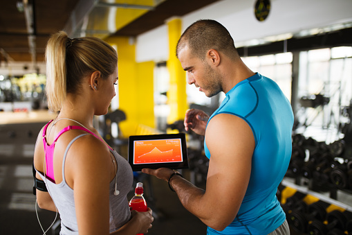 Young sporty woman is  discussing workout plan, progress and statistics with her fitness instructor using digital tablet.