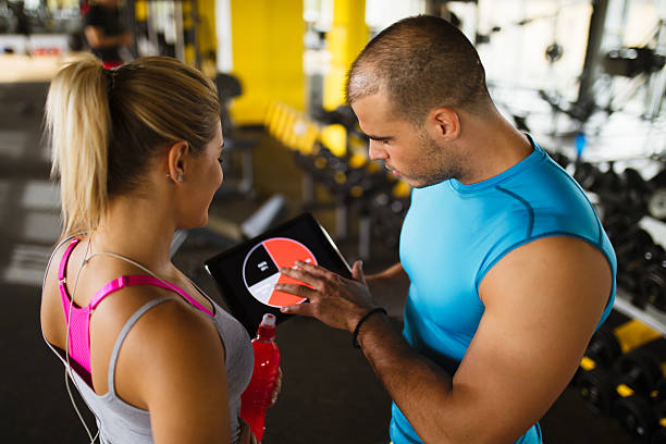 istock Young woman discussing workout progress with fitness instructor 627076242