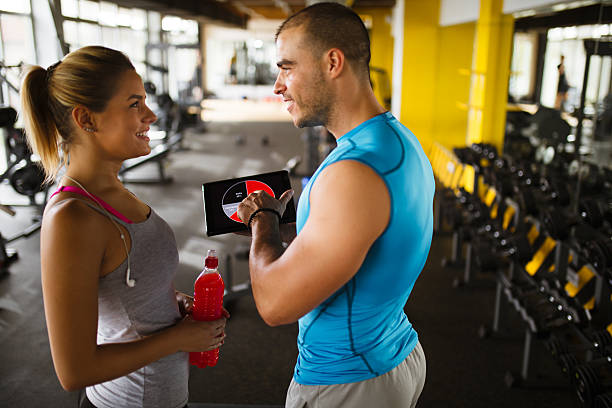 istock Young woman discussing workout progress with fitness instructor 627076276