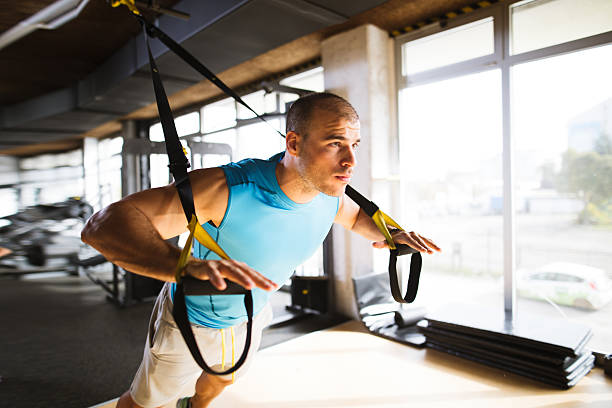 Man doing arm exercises with suspension straps at gym Young athletic man having sports training and doing arm exercises with suspension straps at gym. suspension training stock pictures, royalty-free photos & images