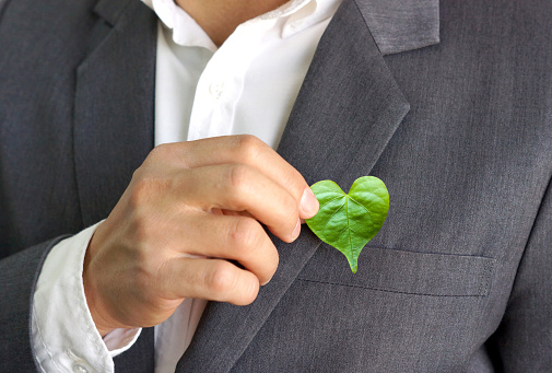 Businessman putting a green leaf with a heart shape from his pocket / Green business / Business with corporate social responsibility and environmental concern