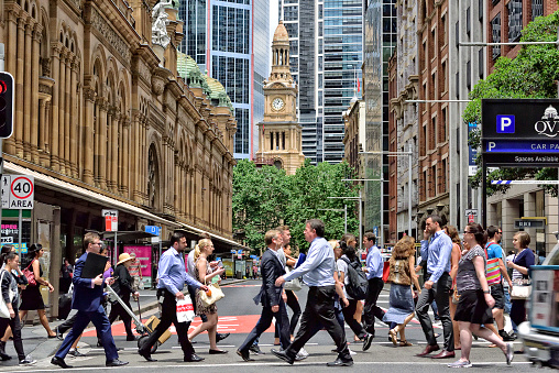 Sydney, Australia - November 12, 2015: People crowd crossing street in central Sydney. Landmark in background, shopping center to the left.