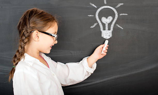 istock Kid in glasses with idea lamp on school chalkboard 627176616