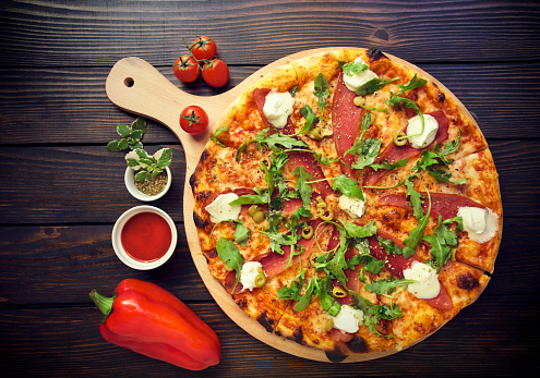 Rustic pizza with salami, olives and basil on wooden table