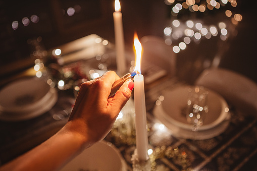 Shot of woman's hand lightening candels on Christmas decorated table. Evening or night.