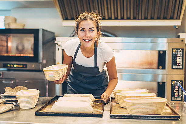 Busy morning in the bakery Young woman working in a bakery preparing the bread for baking. baker occupation stock pictures, royalty-free photos & images