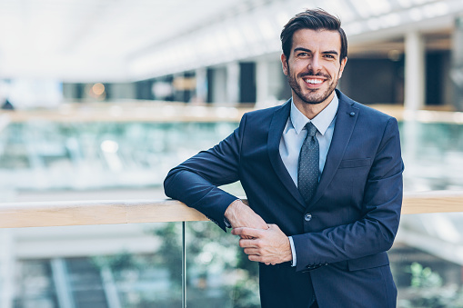 Smiling businessman standing inside modern office office building, with copy space.