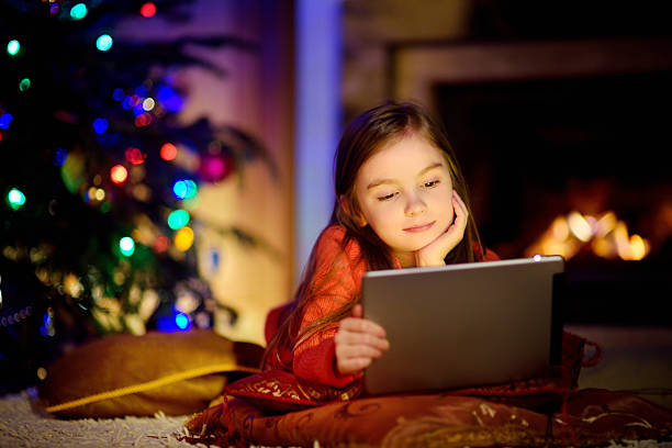 istock Adorable little girl using tablet pc by fireplace on Christmas 627217292