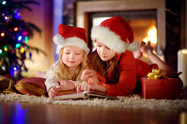 istock Two cute little sisters reading story book under Christmas tree 627217816