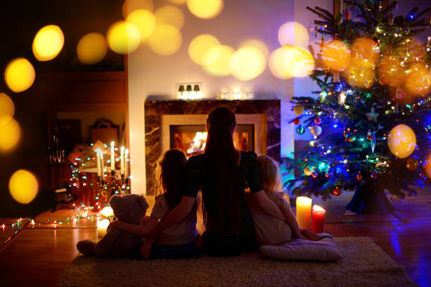 istock Young mother and daughters sitting by a fireplace on Christmas 627217990