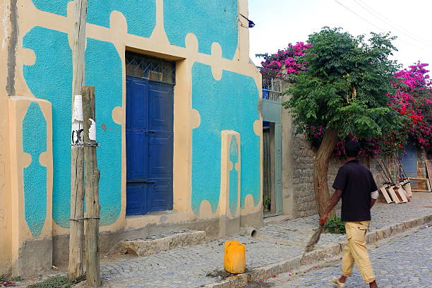 Tigrayan man with cleaning rag in hand. Mekele-Ethiopia. 0440 Mekele, Ethiopia-March 29, 2013: Tigrayan man washes mysterious items inside a yellow plastic bucket on the sidewalk in front of his traditional house with walled orchard-flowering shrubs protruding over-cobblestone pavement and sidewalk. Debubawi zone-Tigray region. kerbstone stock pictures, royalty-free photos & images