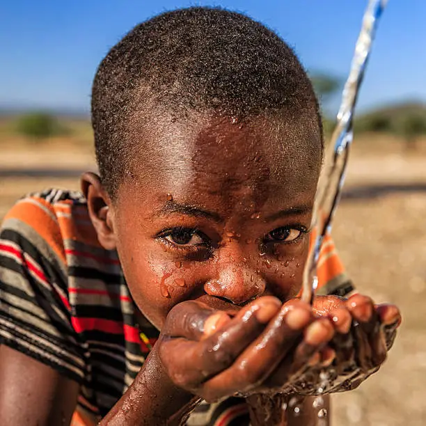 African young boy from Samburu tribe drinking fresh water on savanna.  Potable water is very precious in Africa - women and children often walk long distances through the savanna to bring back jugs of water that they carry on their back. 