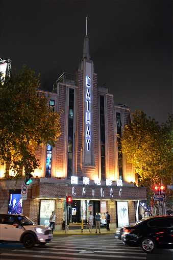 Shanghai, China - September 27, 2016: Exterior of Cathay Cinema by night, one of Shanghai’s great Art Deco Cinemas, first opened on January 1, 1932. Huaihai road, Shanghai. People in the background, standing outside the Cinema.