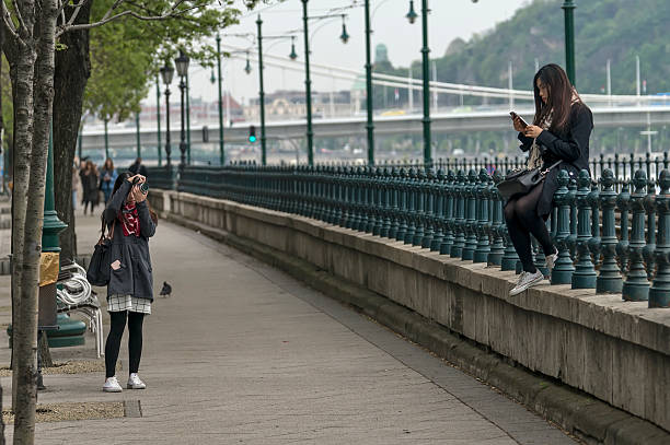 Budapest, Hungary - April 11, 2016: A young Chinese girl sitting on the fence and play with mobile phone.