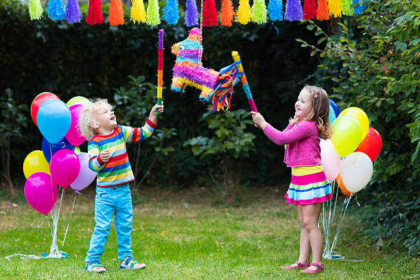 Kids playing with birthday pinata and balloons Kids birthday party. Group of children hitting pinata and playing with balloons. Family and friends celebrating birthday outdoors in decorated garden. Outdoor celebration with active games. toddler hitting stock pictures, royalty-free photos & images