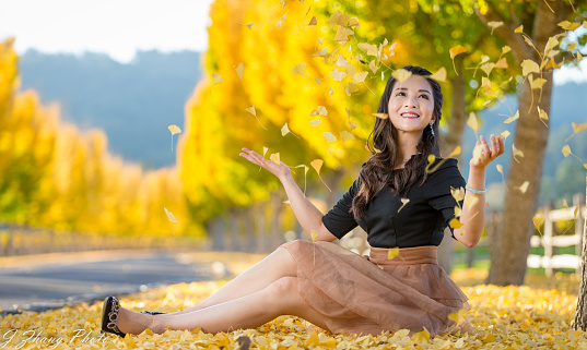 Ginkgo tree on the backgoud, One smiling Asian girl sitting on the ground and playing the leaves.