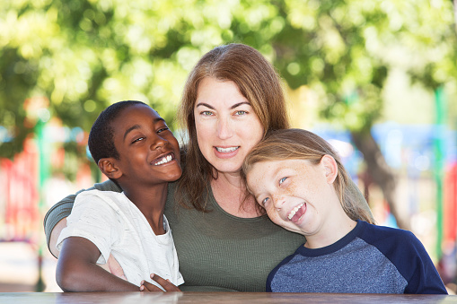Joyful single parent sitting in between adopted child and son at table in park