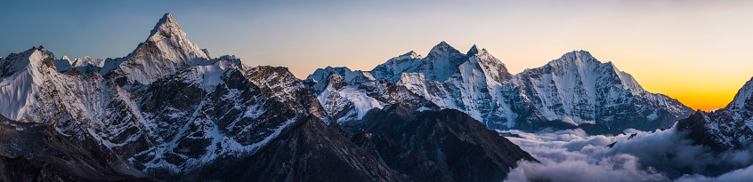 Delicate sunset light illuminating the dramatic snow capped summits and fluted glaciers high above the clouds of the Khumbu valley, from the iconic spire of Ama Dablam (6812m) to the pinnacles of Kangtega (6782m) and Thamserku (6623m) deep in the Everest National Park of Nepal, a UNESCO World Heritage Site.