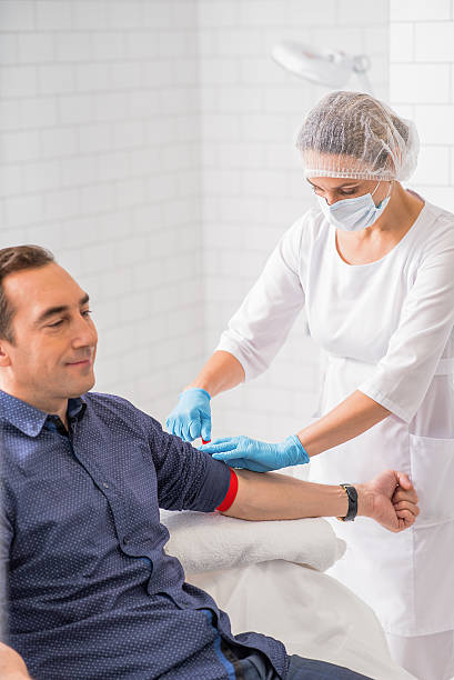 Middle-aged man preparing for blood-test Professional doctor is wearing elastic band on male arm before blood sampling. Patient is sitting and smiling patient blood management stock pictures, royalty-free photos & images