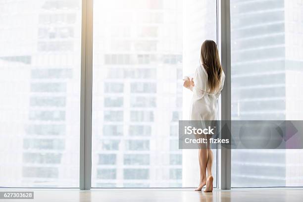 Young Woman Near The Floor Window Stock Photo - Download Image Now - Women, Looking Through Window, Luxury