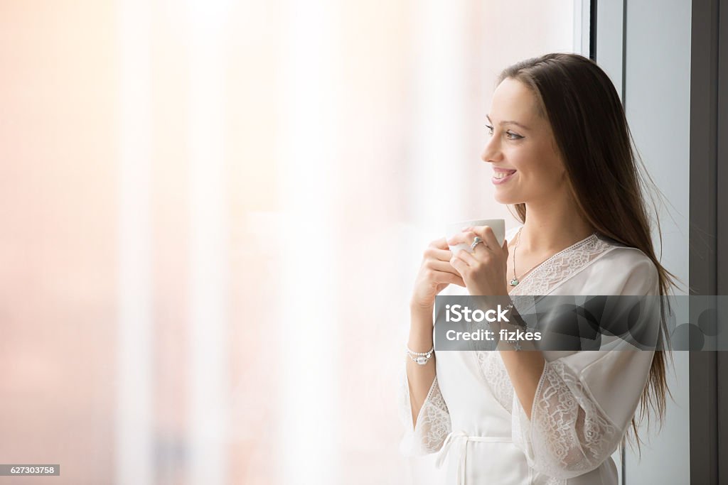 Jeune femme heureuse debout près de la fenêtre - Photo de Admirer le paysage libre de droits