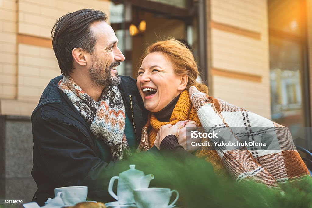 Man and woman dating in cafe Happy middle-aged couple is relaxing in cafeteria outdoors. They are hugging with love and laughing Mature Couple Stock Photo