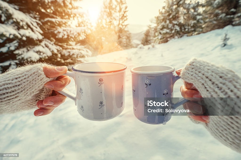 Couple hands with mugs with hot tea in winter forest Couple hands in mittens take a mugs with hot tea in winter forest Adult Stock Photo