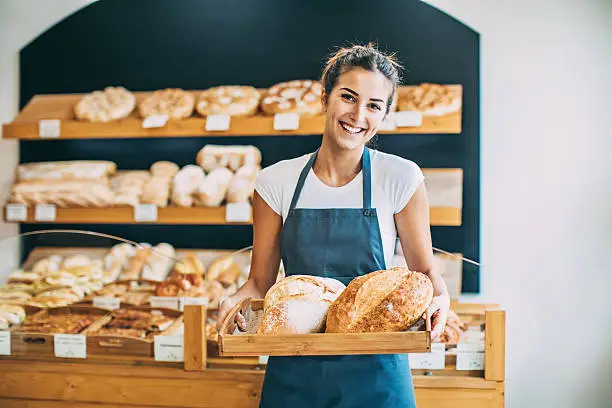 Young bakery owner holding a tray with bread, with copy space.