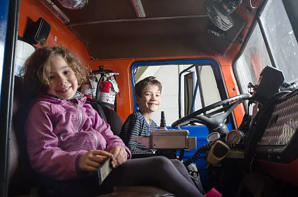 Photo of Two kids sit in firetruck with big smile