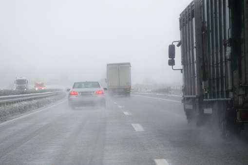 cars, trucks and a rescue vehicle driving in dangerous winter weather with poor visibility during snow and rain on the highway, concept for safety in traffic, copy space