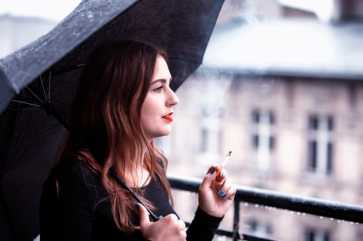 portrait of brunette young woman holding an umbrella and smoking a cigarette