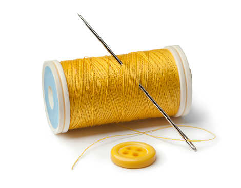 Yellow bobbin, needle and sewing button on white background