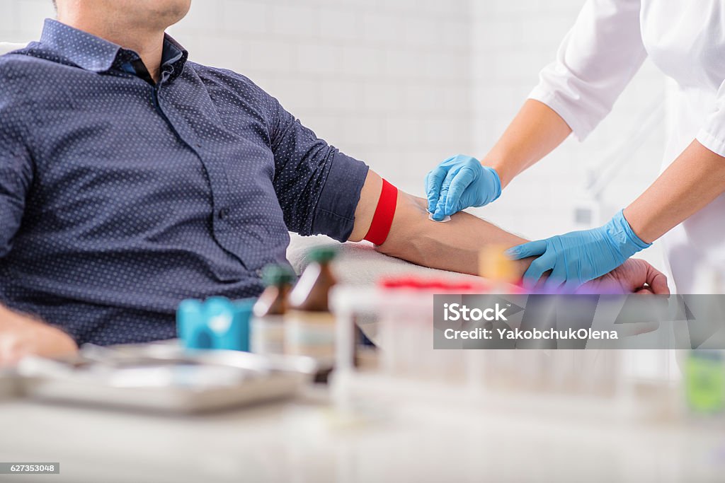 Professional doctor preparing patient for procedure Close up of nurse disinfecting male arm before blood test. Man is sitting on chair near medical set Blood Donation Stock Photo